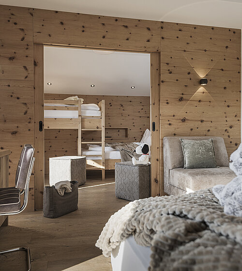 Familienfreundliches Zimmer mit Schreibtisch, Sofa und Durchgang zum Kinderbereich mit Etagenbetten im Hotel Bachmanngut Wolfgangsee