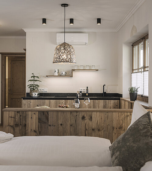 Küchenzeile mit Hängelampe, Naturholzfronten und dekorativer Tanne neben dem Bett im Familienappartement Hotel Bachmanngut Wolfgangsee