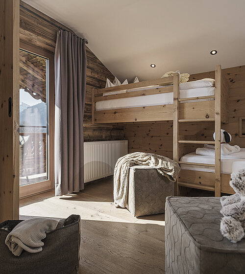 Kinderzimmer mit Holzstockbetten, Kuscheltieren und Zugang zum sonnigen Balkon mit Bergblick im Hotel Bachmanngut Wolfgangsee